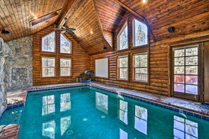 A log cabin with a large indoor swimming pool, stone walls, and large windows.