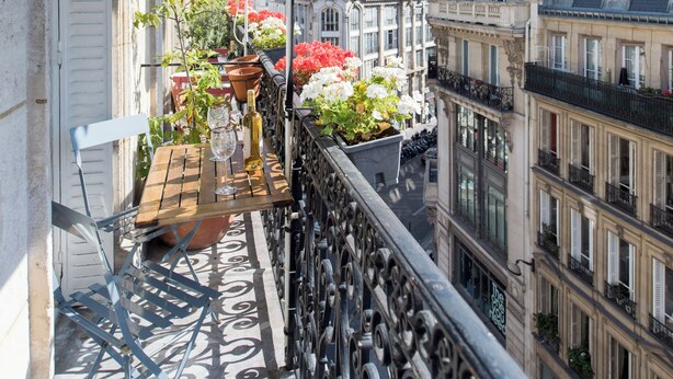 Un balcon agrémenté d’un parasol vert, de plantes en pot et d’une table en bois.