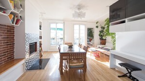 Un vaste salon doté d’une table à manger en bois, de sièges confortables, d’une cheminée et de grandes fenêtres offrant une vue sur l’extérieur.