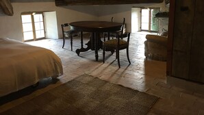 Een rustieke kamer met houten plafond, een ronde tafel met stoelen, een bed en een raam.