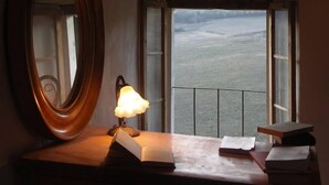 Een kamer met een grote spiegel, een nachtkastje met een lamp en uitzicht op een wateroppervlak door een raam.