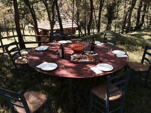 Une table de salle à manger ronde, installée à l’extérieur, avec des chaises, des assiettes, des verres et une bouteille.