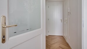 A hallway with a wooden floor and white walls, leading to a closed door.
