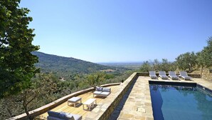 Ein Poolbereich mit Steinmauern und Liegestühlen, mit Blick auf eine malerische Landschaft.
