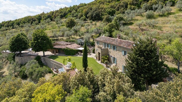 Eine steinerne Villa mit Ziegeldach, umgeben von üppiger Vegetation und Bäumen.