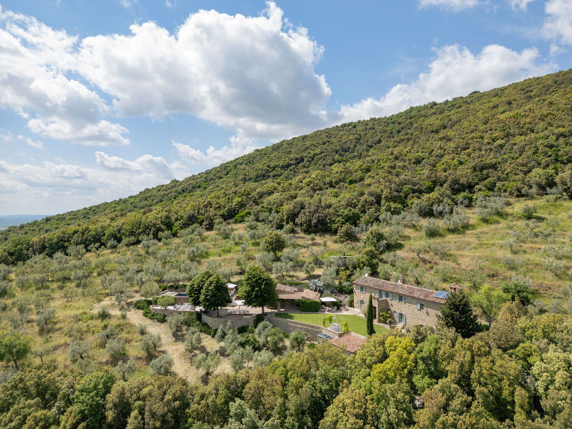 Une propriété située sur une colline, avec des bâtiments en pierre, un mur de pierre et un jardin bien entretenu.