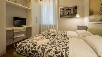 Ein Hotelzimmer mit einem Bett, einem Schreibtisch mit Fernseher, einem Sessel, einem Fenster mit Vorhängen und einem Bild an der Wand.