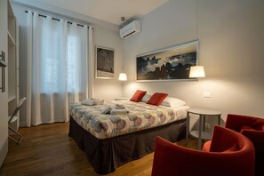 Ein Hotelzimmer mit einem Bett, zwei roten Stühlen, einem kleinen Tisch und Kunstwerken an den Wänden.