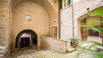 Un cortile in pietra con un ingresso ad arco, piante in vaso e un piccolo tavolo.