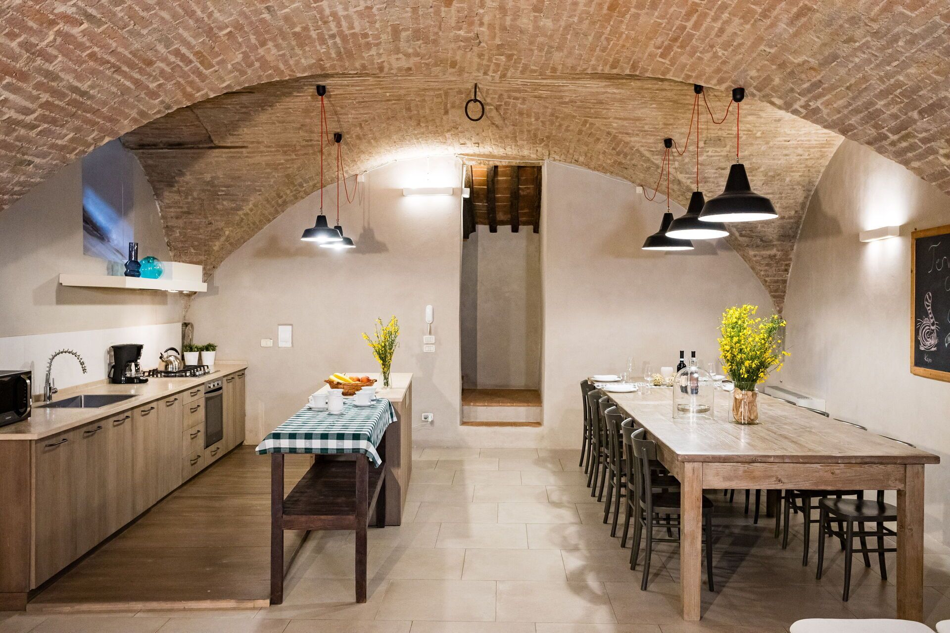 Una cucina rustica con pareti in mattoni a vista, un tavolo da pranzo in legno e illuminazione a sospensione.
