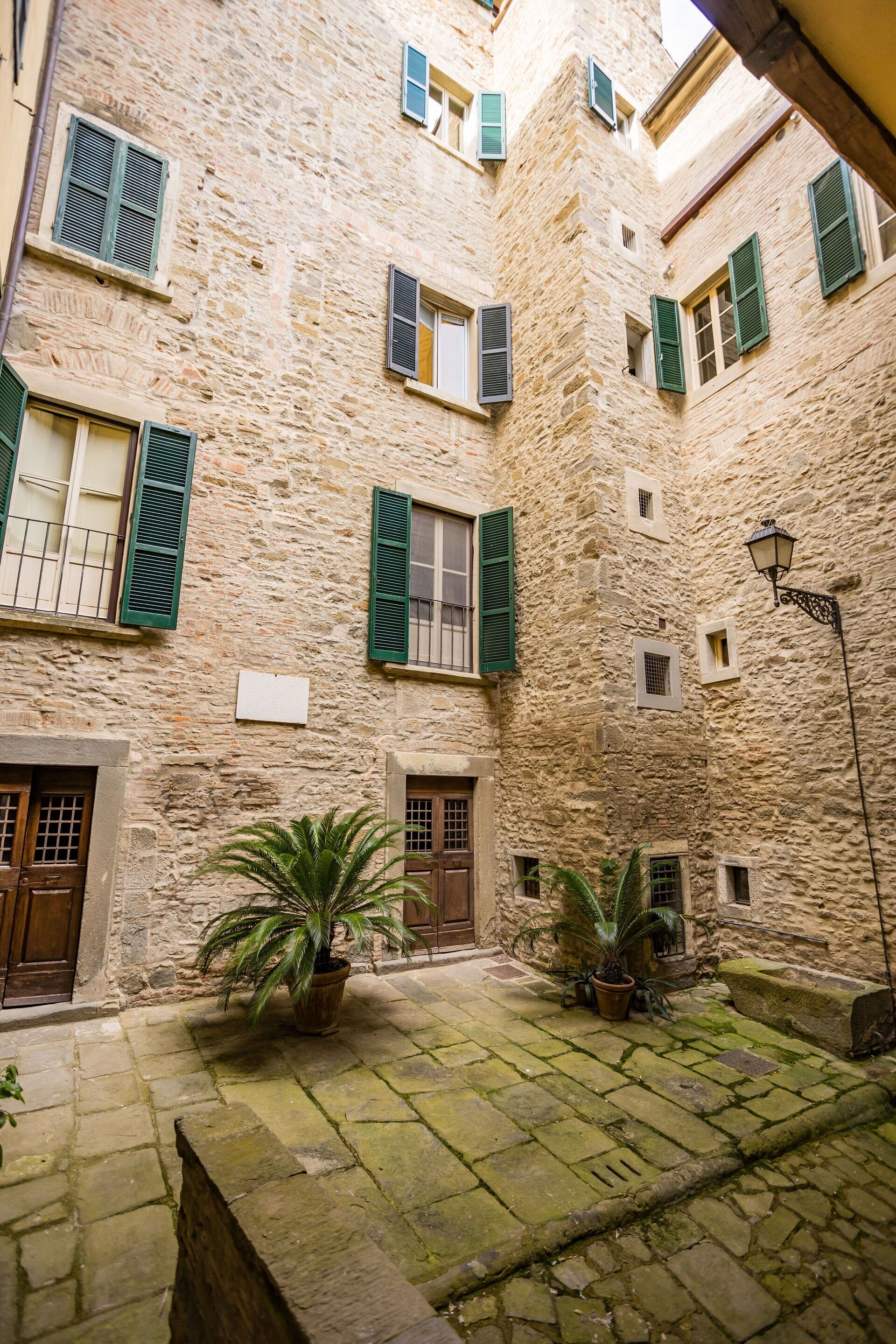 Un cortile con mura in pietra, persiane verdi e piante in vaso.