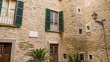 Un cortile con mura in pietra, persiane verdi e piante in vaso.