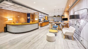 Eine moderne Hotelhalle mit einer gebogenen Rezeption, einem Essbereich mit Tischen und Stühlen sowie einem dekorativen Wandbild.
