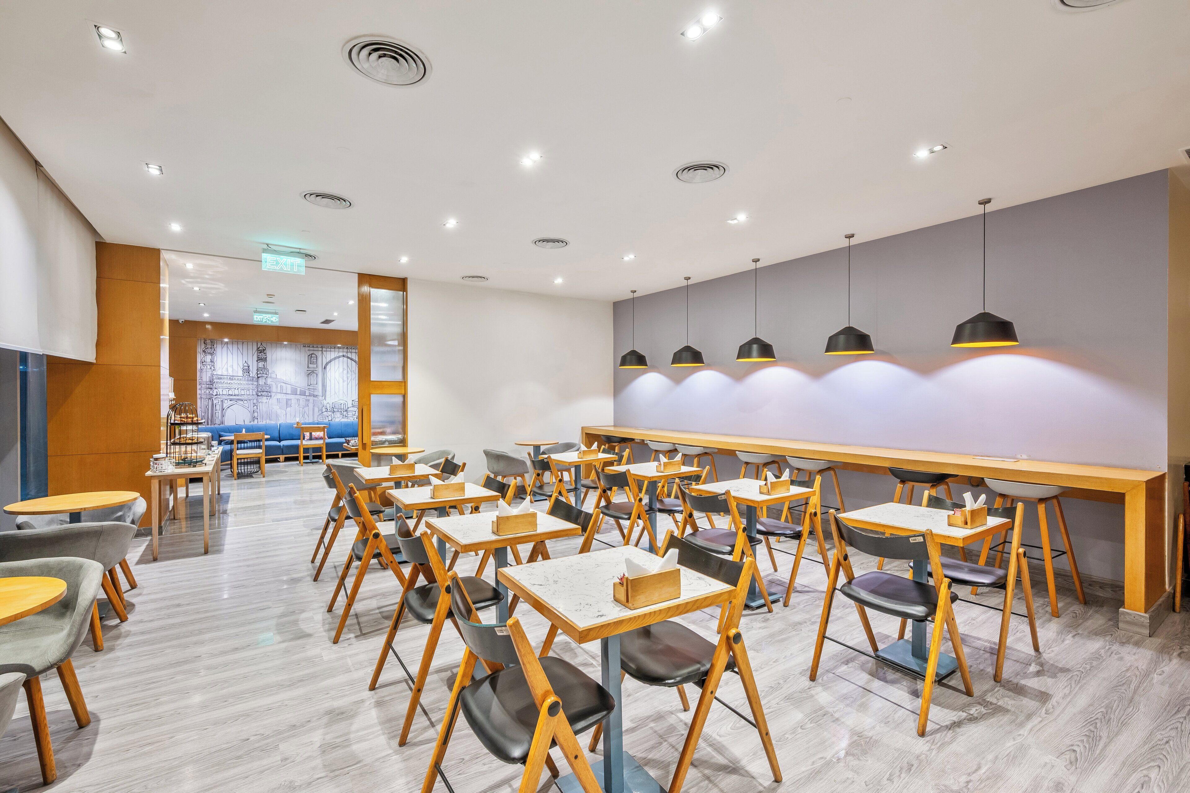 A modern dining area with tables and chairs, a long counter, and pendant lights.