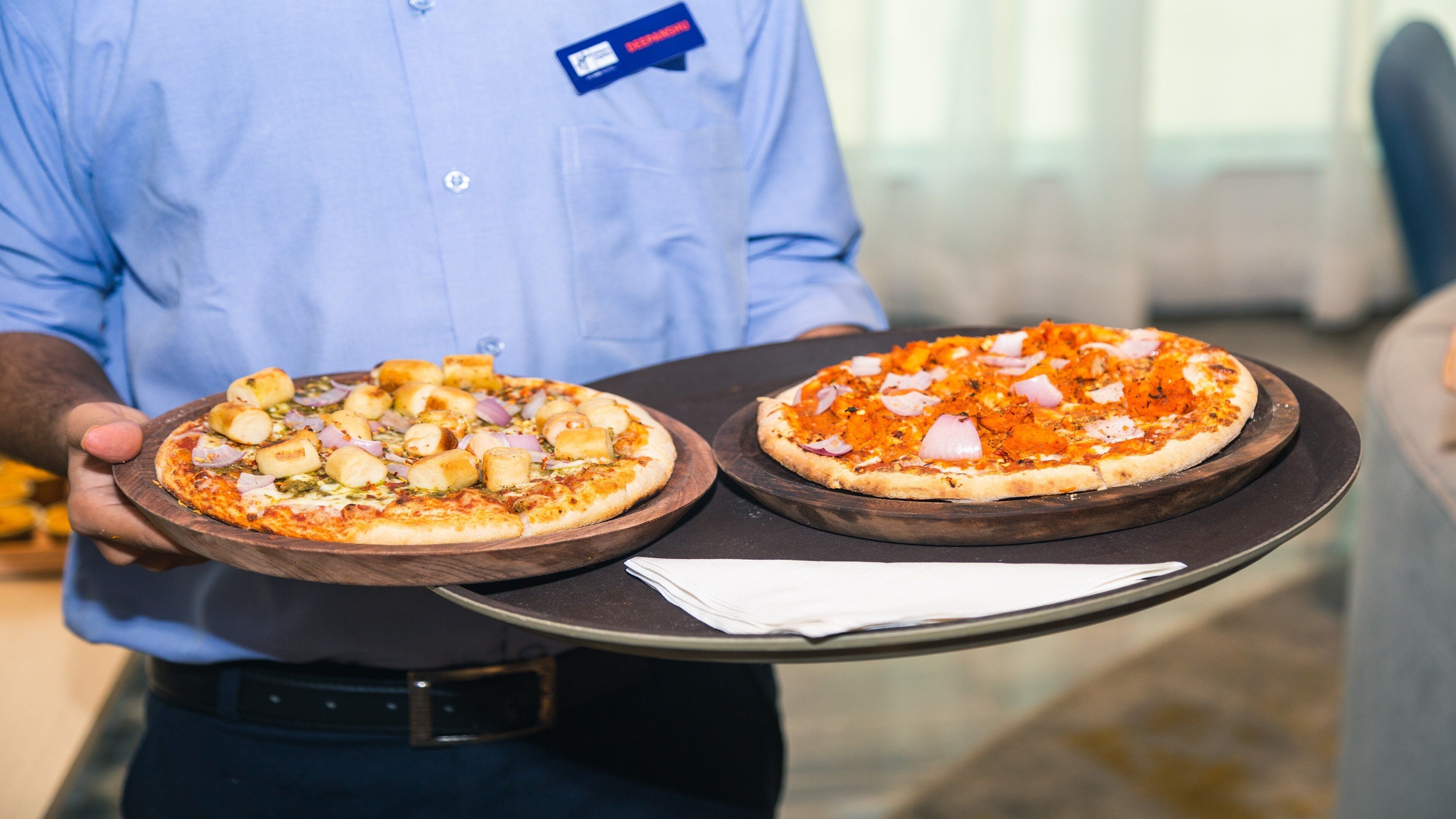 A person holding two pizzas on wooden boards.
