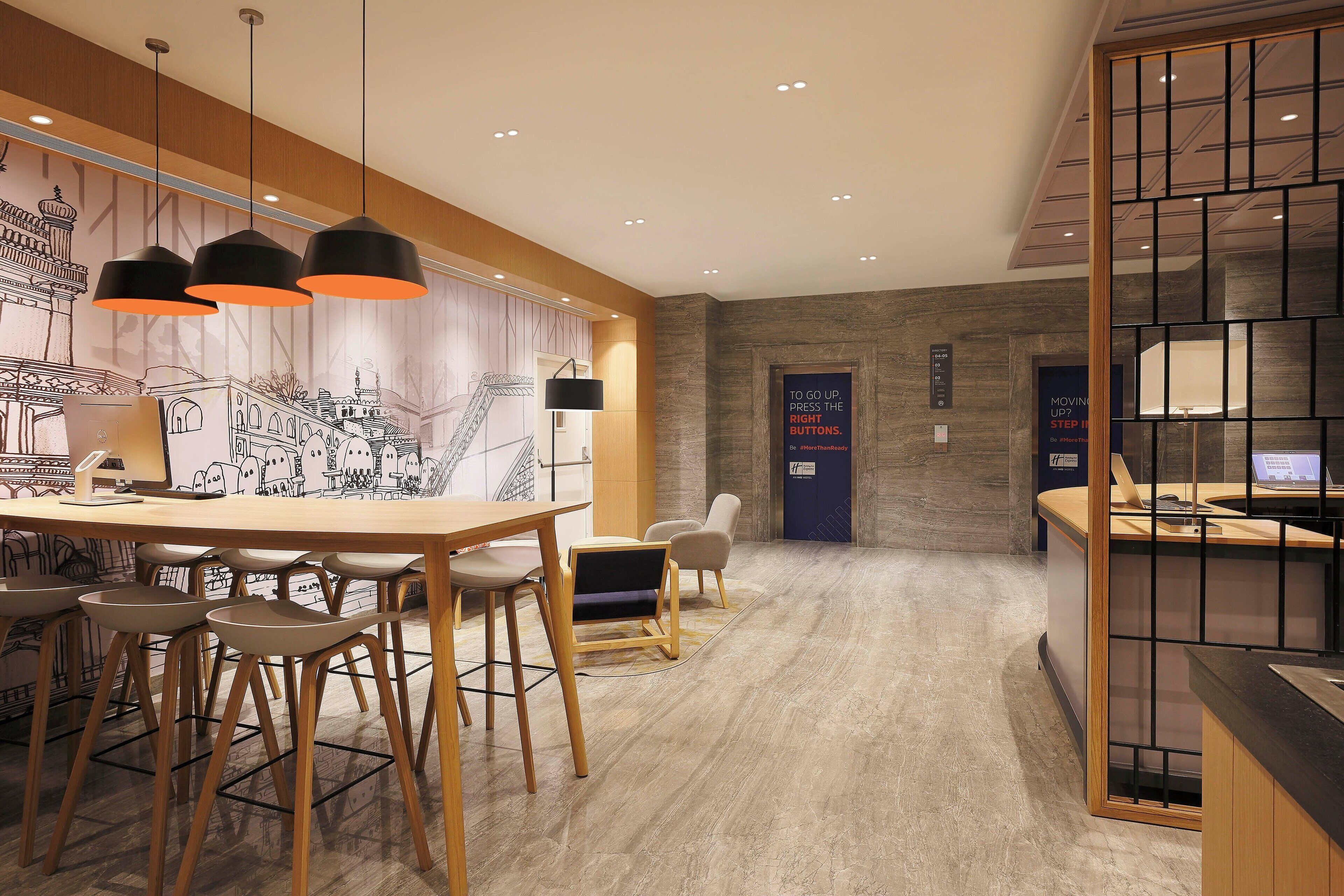 Un hall d’hôtel moderne avec un comptoir d’accueil en bois, un espace repas doté d’une grande table et de chaises, et une fresque murale.