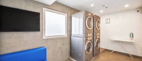 Un cuarto de lavandería con un banco azul, lavadora y secadora empotradas en la pared, y una plancha pequeña.