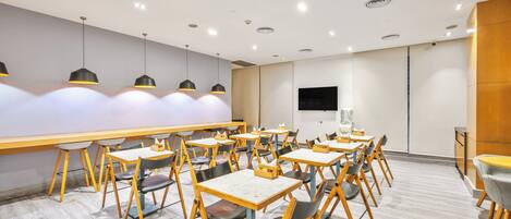 A modern dining area with tables and chairs, recessed ceiling lights, and a wooden accent wall.