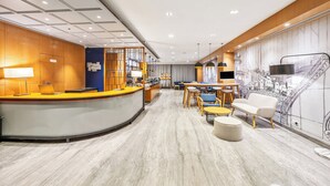 Eine moderne Hotelhalle mit einer gebogenen Rezeption, einer Sitzecke mit Tischen und Stühlen sowie einem großen Wandbild.