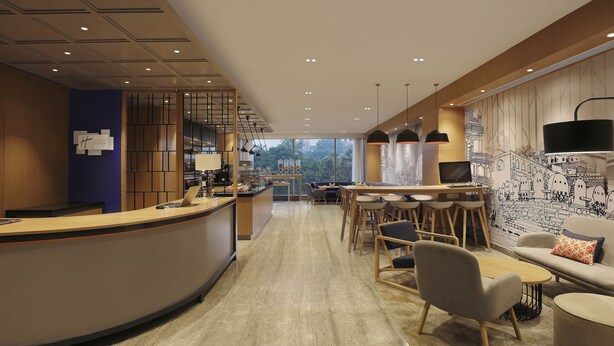 Eine moderne Hotelhalle mit einer gebogenen Rezeption, einer Sitzecke mit Tischen und Stühlen sowie einem großen Wandgemälde.