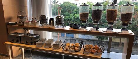 A coffee station with multiple coffee dispensers, a toaster, and a display of pastries.