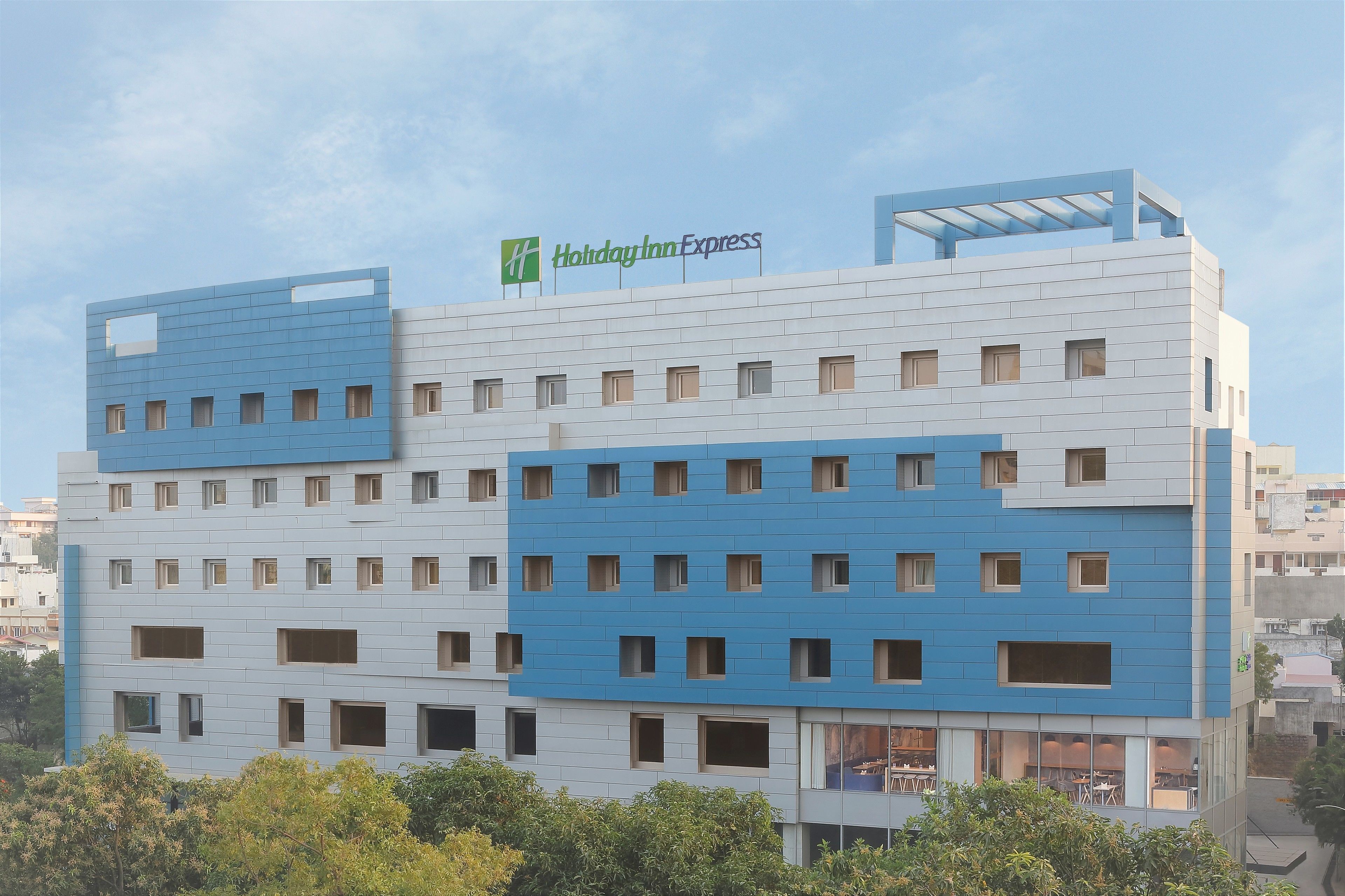 Un hotel Holiday Inn Express con diseño moderno, que presenta una combinación de paneles azules y blancos en el exterior, numerosas ventanas y un techo plano.