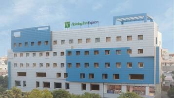 Un hotel Holiday Inn Express con diseño moderno, que presenta una combinación de paneles azules y blancos en el exterior, numerosas ventanas y un techo plano.