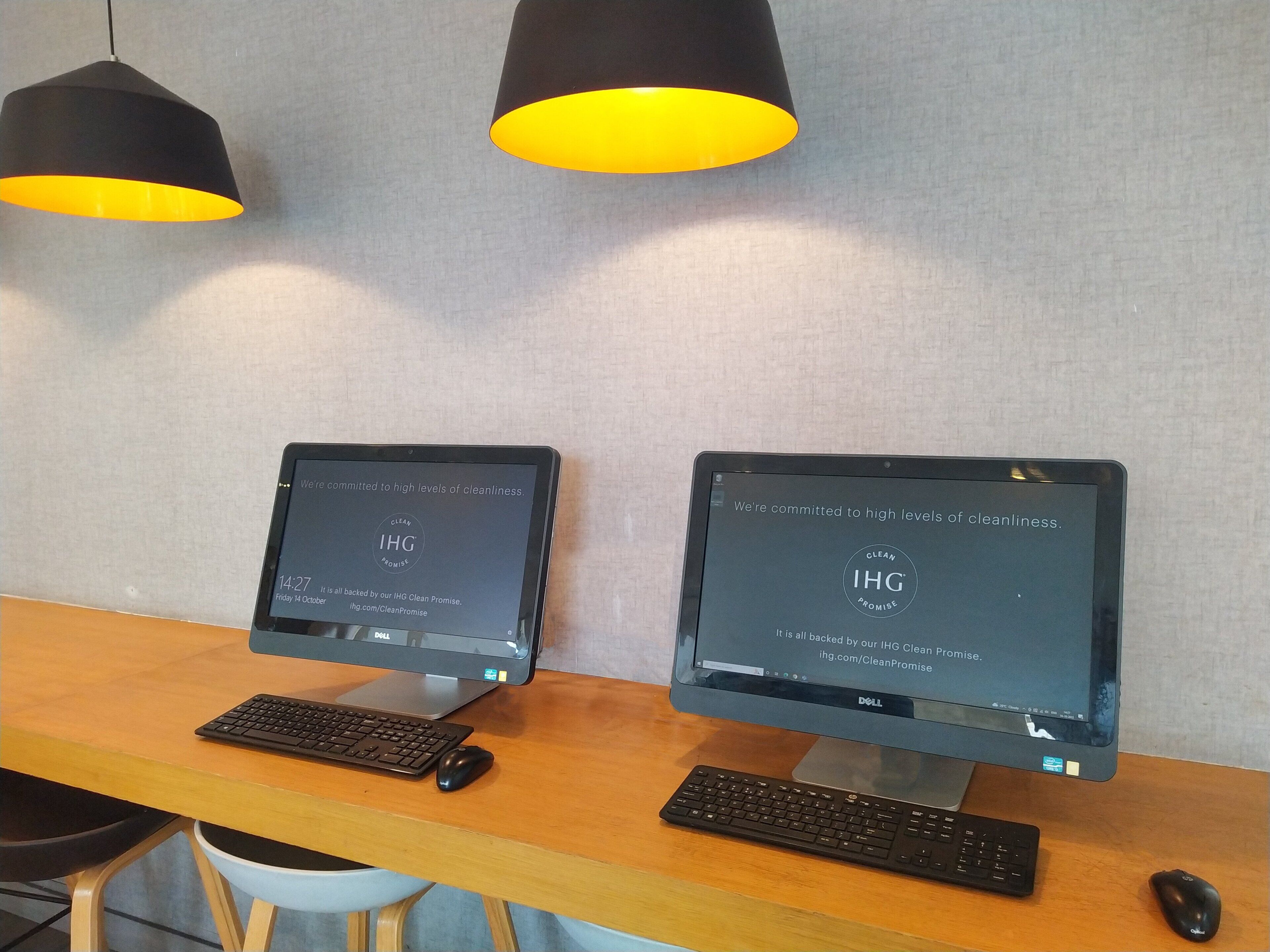 Dois computadores de mesa sobre uma escrivaninha de madeira, com teclado e rato na frente de cada um.