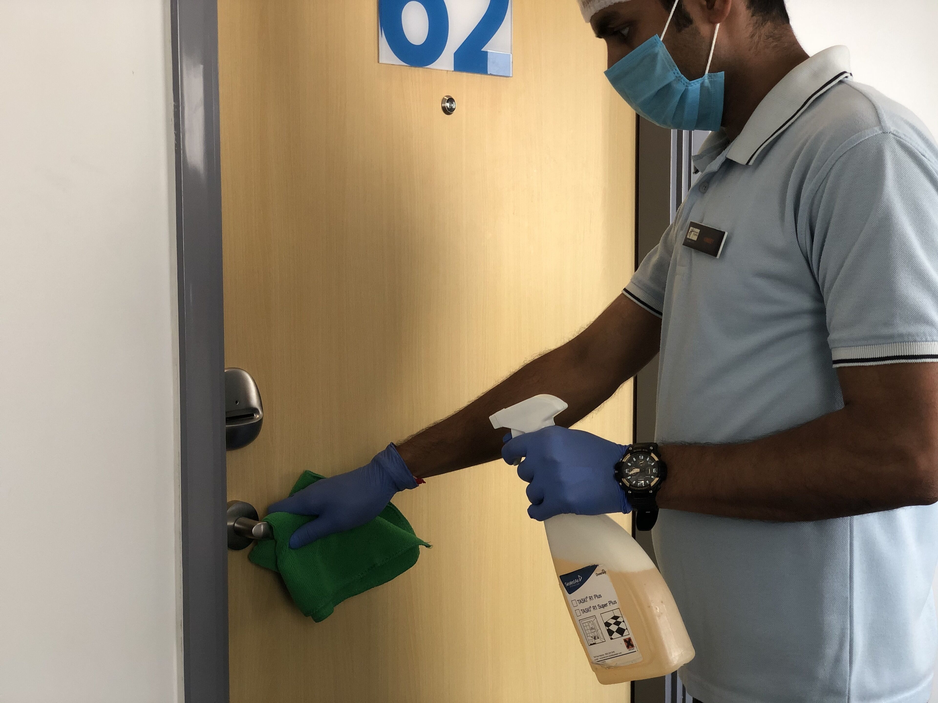 A person cleaning a door handle with a spray bottle and a green cloth.