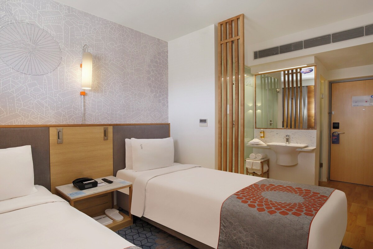 Een hotelkamer met twee bedden, een bureau, een spiegel, een wastafel en een douche.