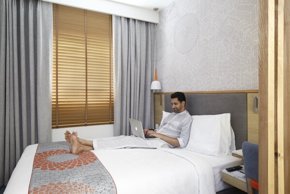 A hotel room with a bed, a laptop, a bedside table, and a window with blinds. - Holiday Inn Express Hyderabad Banjara Hills by IHG (Hyderabad)
