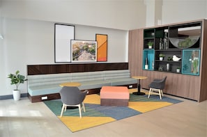 A modern lounge area with a sofa, two armchairs, a small table, and a bookshelf.