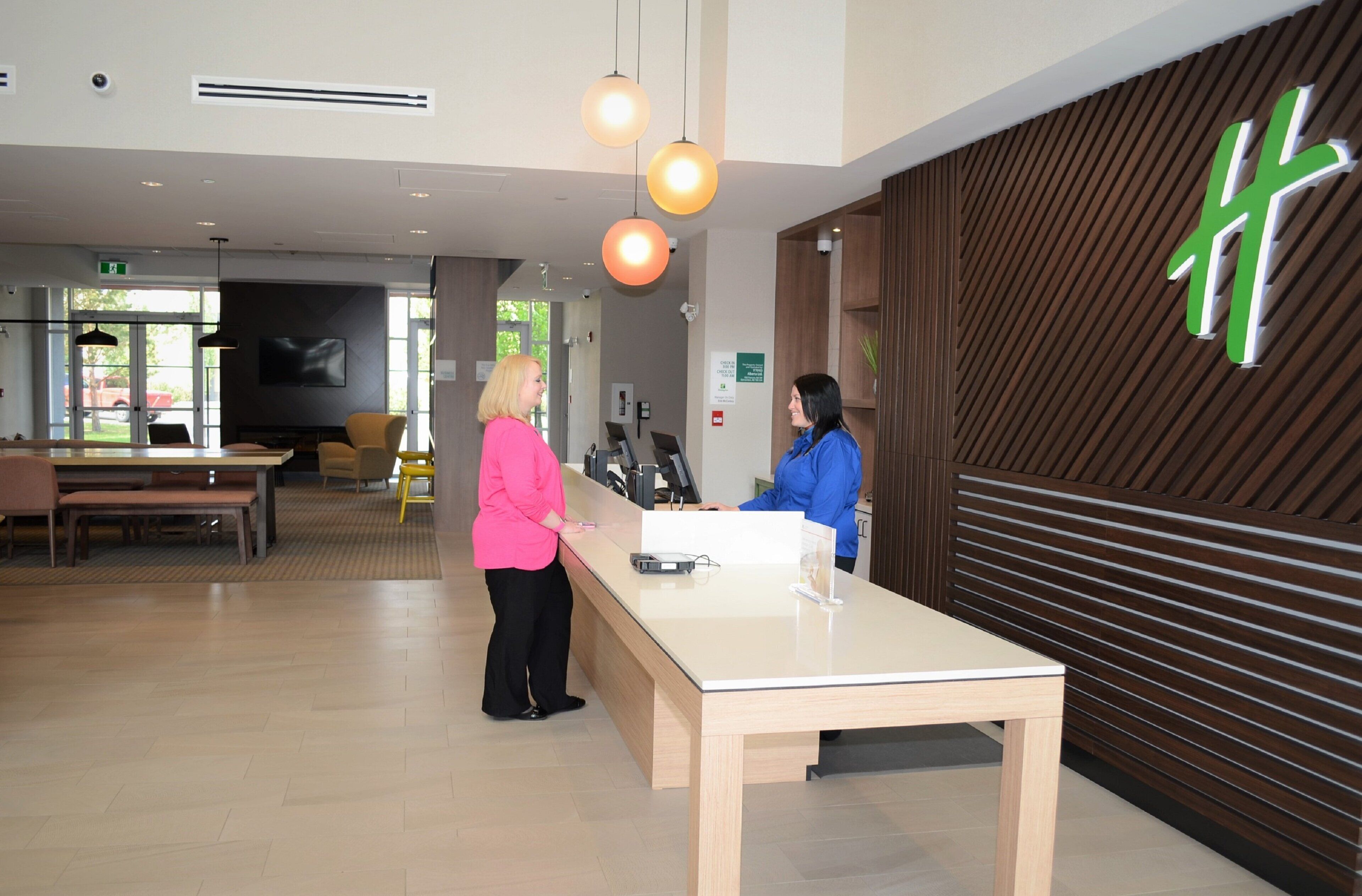 A reception area with a reception desk, two people interacting, a television, and a sign with a green logo on the wall.