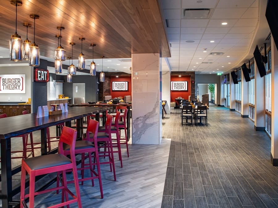 Interior moderno de restaurante com várias mesas e cadeiras, iluminação pendente e um suporte de menu visível.