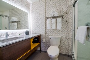 A modern bathroom with a patterned wallpaper, a large mirror, a toilet, a sink with a wooden vanity, and a glass shower enclosure.