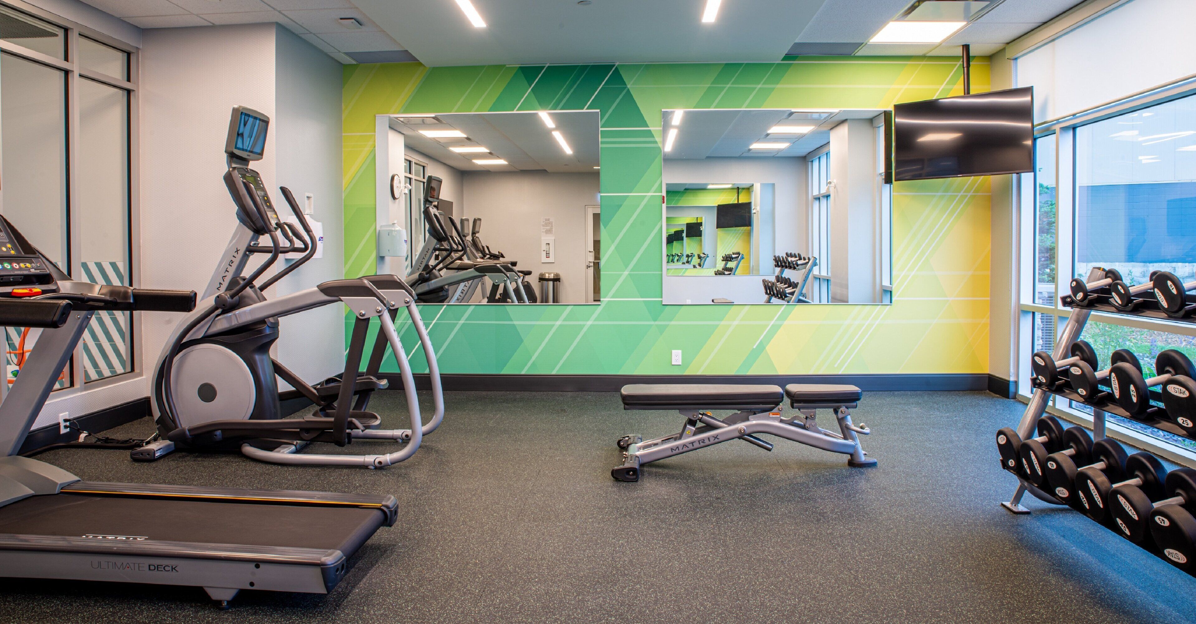 Une salle de sport équipée de machines de cardio, d’une zone pour la musculation et d’un miroir qui reflète l’espace.