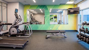 Une salle de sport équipée de machines de cardio, d’une zone pour la musculation et d’un miroir qui reflète l’espace.