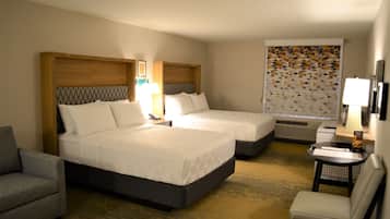 Habitación de hotel con dos camas, un sofá, una silla, una mesita y un televisor fijado a la pared.