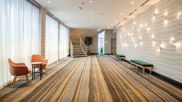 A hotel lobby with a striped carpet, a staircase, a reception desk, and a seating area.