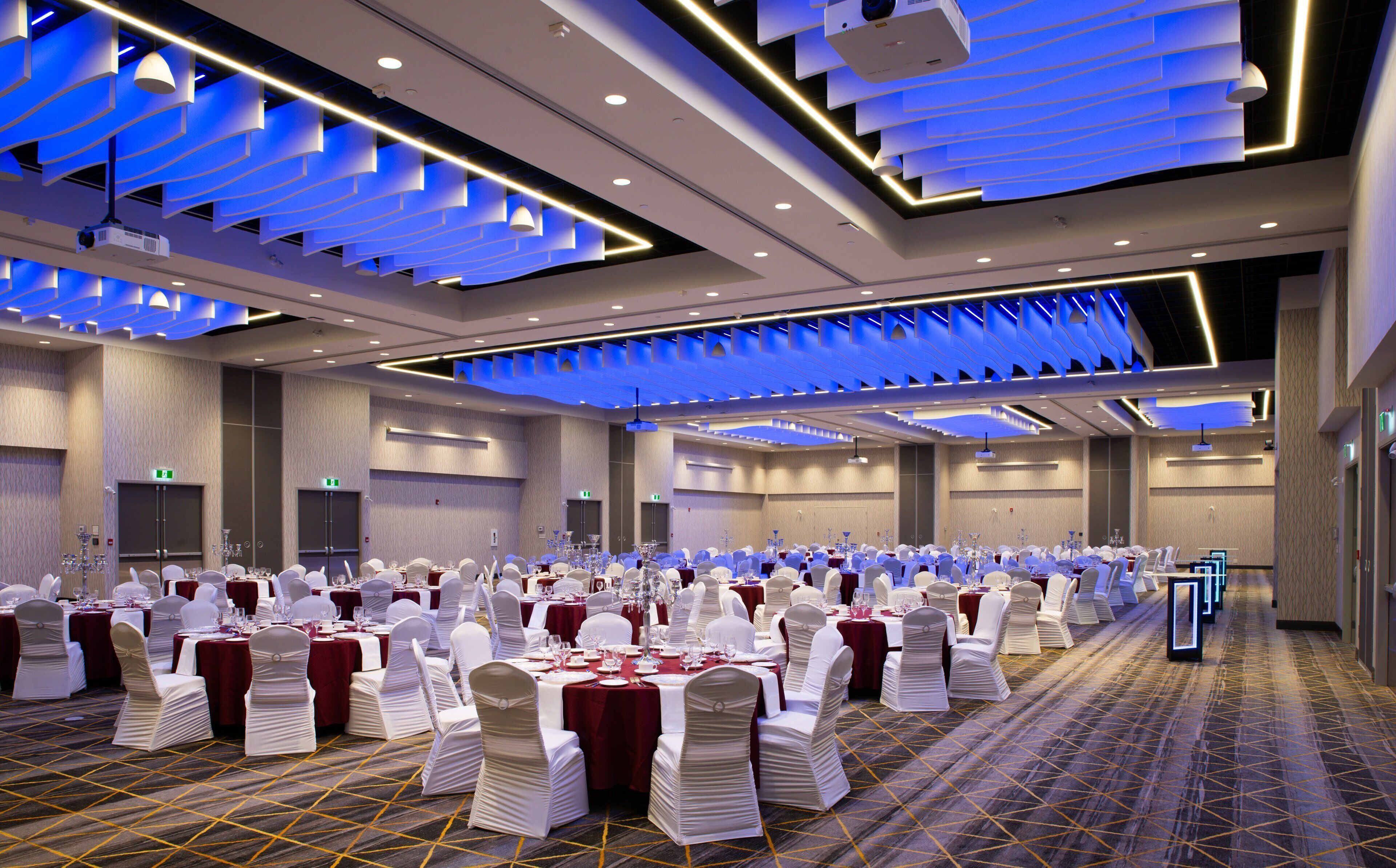 Une vaste salle de banquet avec de longues rangées de tables rondes, des chaises blanches et des nappes rouges.