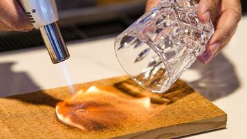 A person holding a glass with a textured pattern, positioned over a wooden surface.