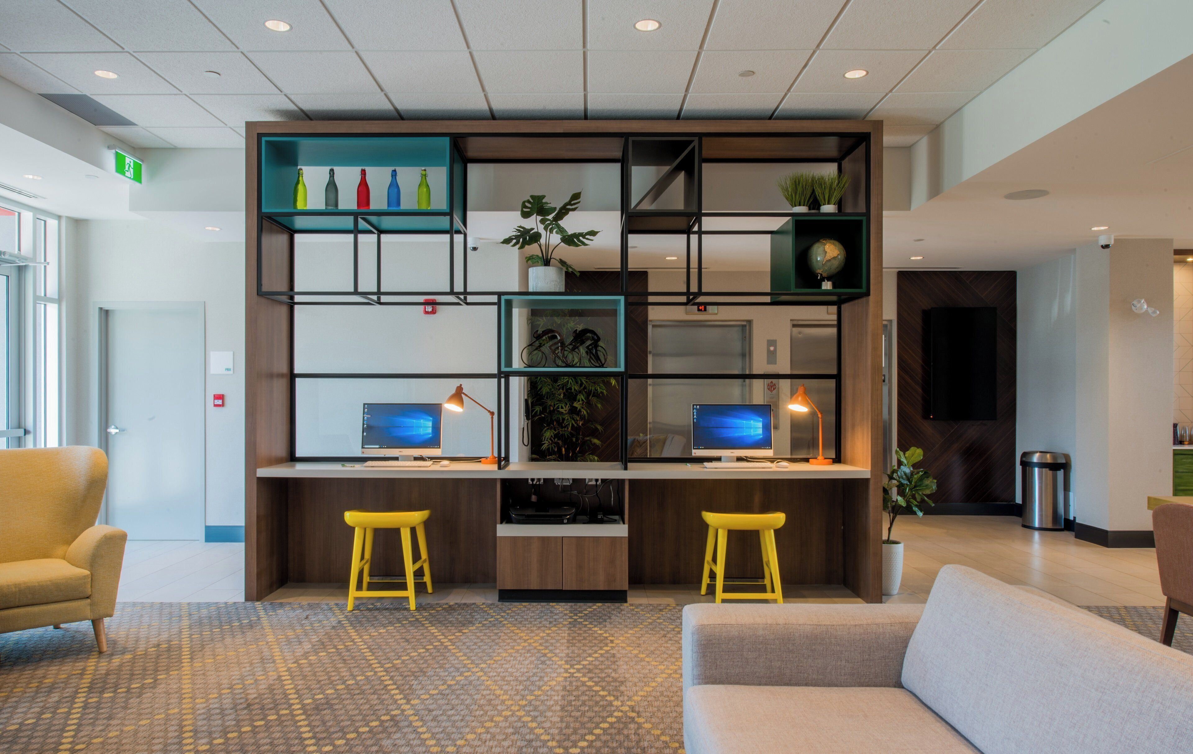 A modern office space with two desks, two yellow stools, a sofa, and a patterned carpet.