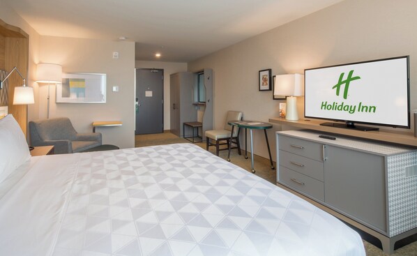 A hotel room with a large bed, a desk with a chair, a television, and a minibar.