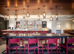 A restaurant with a long counter, red chairs, hanging pendant lights, and a bar area with shelves of bottles.