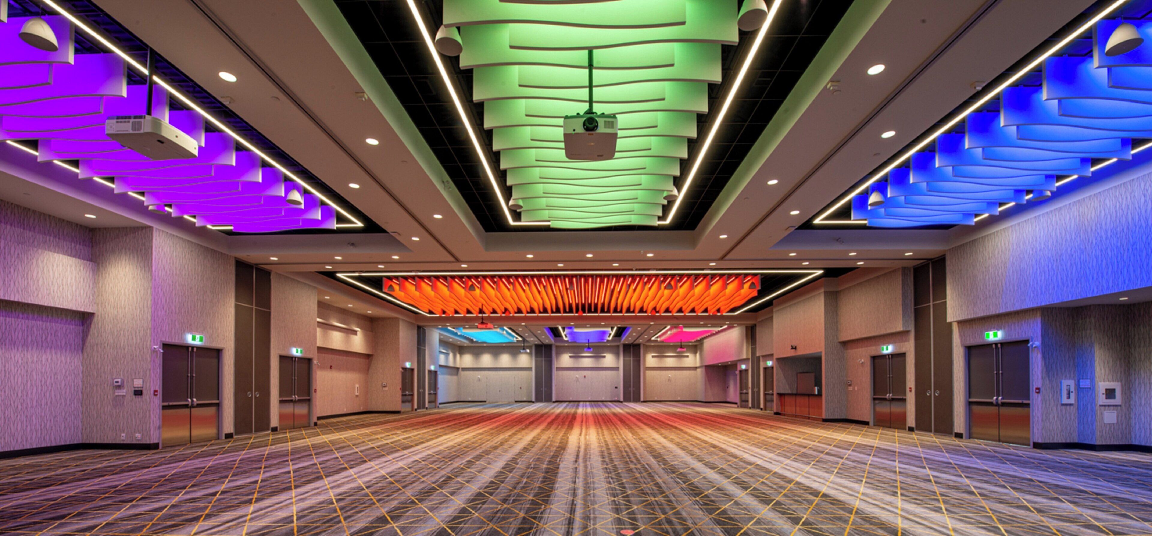 Un amplio vestíbulo de hotel con alfombra estampada, varias puertas e iluminación geométrica en el techo.