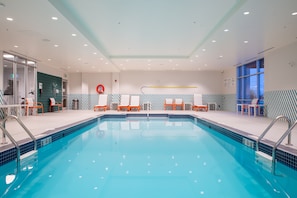 An indoor swimming pool with clear water, surrounded by lounge chairs and a tiled wall.
