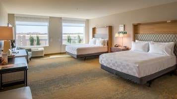 A hotel room with two beds, a desk, a chair, a lamp, and a view of the cityscape.