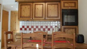 A kitchen with wooden cabinets, a tiled backsplash, and a dining table with chairs. - Very nice apartment skis Chamonix Valley (Les Houches)