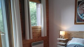 A bedroom with a wooden headboard, a bed with patterned bedding, a bedside table with a lamp, and a window with curtains. - Very nice apartment skis Chamonix Valley (Les Houches)