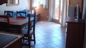 A room with a wooden table and chairs, a sofa, a TV on a wooden cabinet, and a sliding glass door leading to an outdoor area. - Very nice apartment skis Chamonix Valley (Les Houches)
